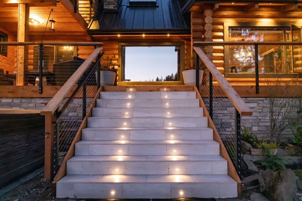 Illuminated steps leading to rustic log cabin entrance.