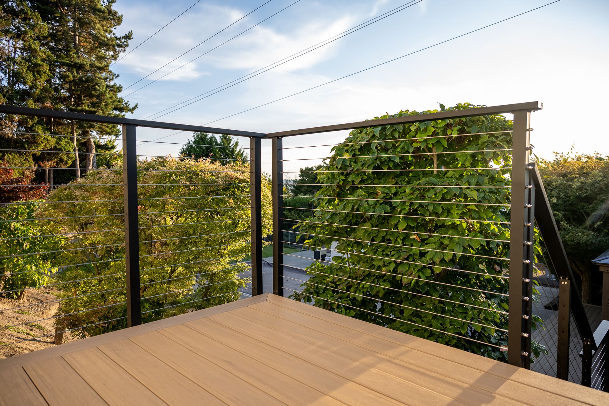 Modern deck with cable railing and green trees.