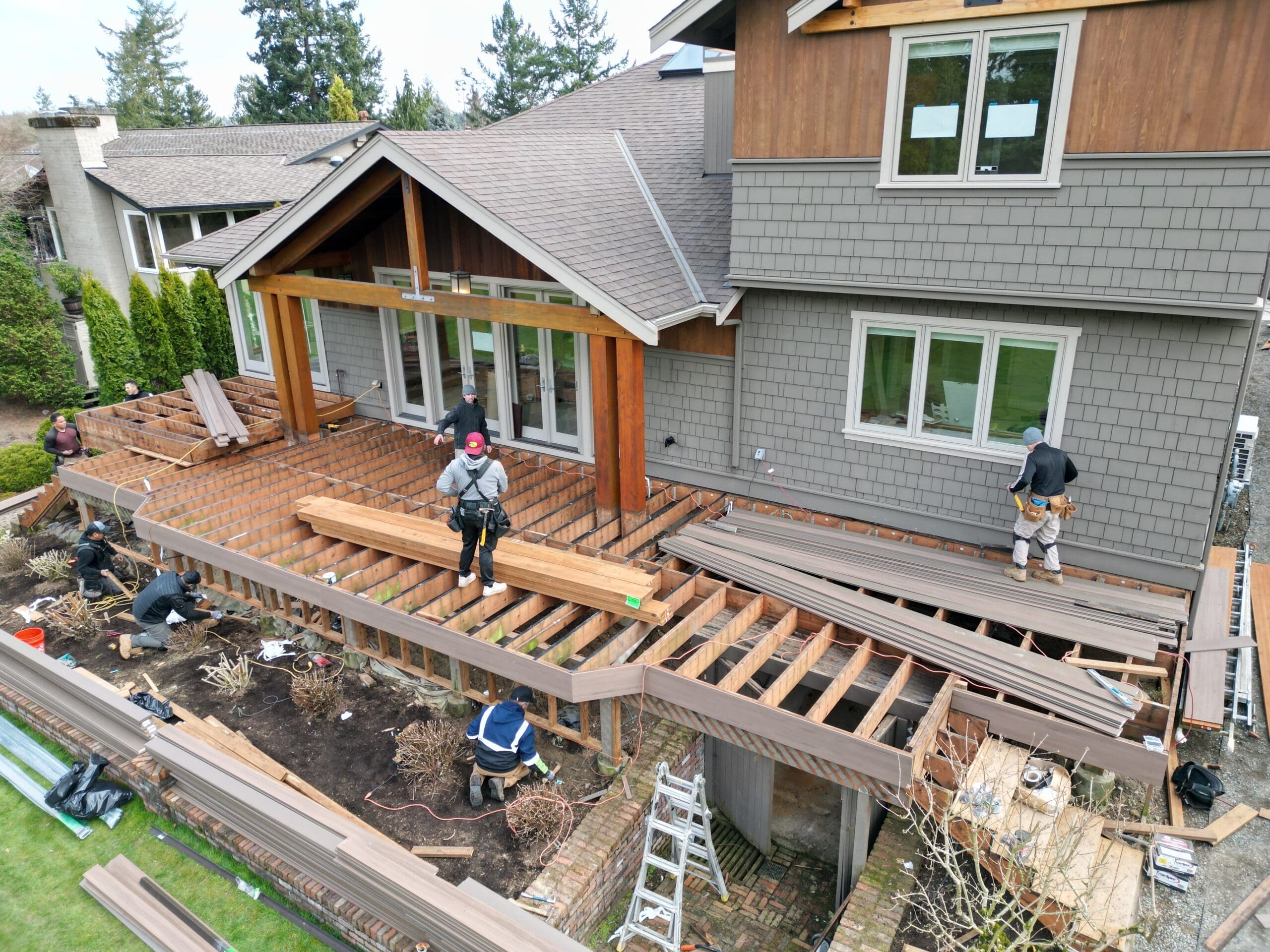 Workers constructing house deck with wooden beams.