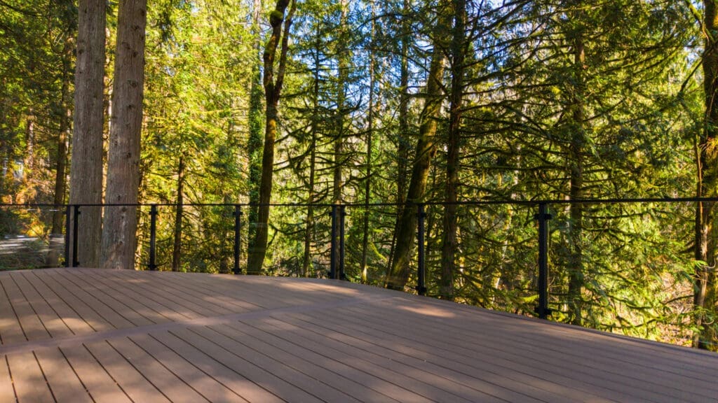 Wooden deck overlooking lush forest with glass railing