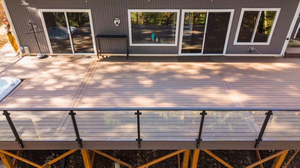 Elevated wooden deck with glass railing behind house