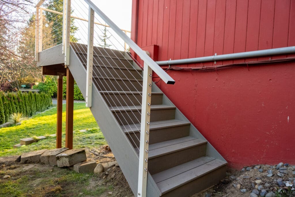 Outdoor wooden staircase with cable railing beside red building